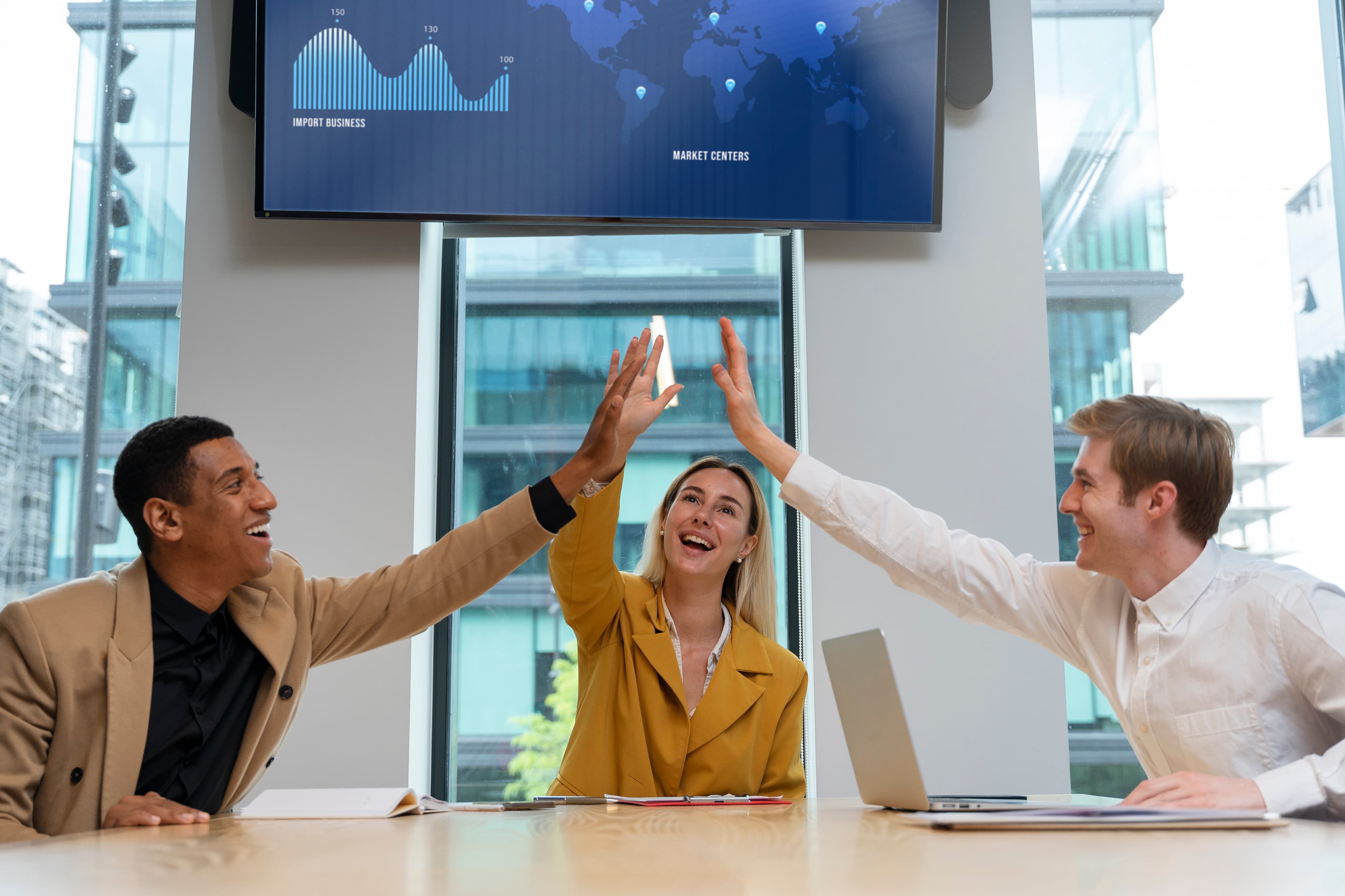 A group of workers celebrate their success by giving high five in the meeting room.