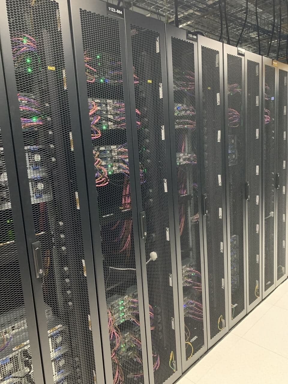 Server rack cabinets with perforated mesh doors showing detailed network cabling and green status indicator lights