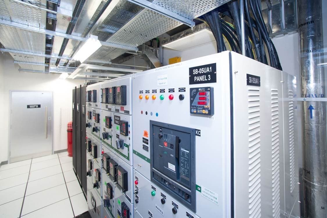 Power distribution unit panel with circuit breakers, digital monitoring displays, and colored indicator lights in clean data center environment