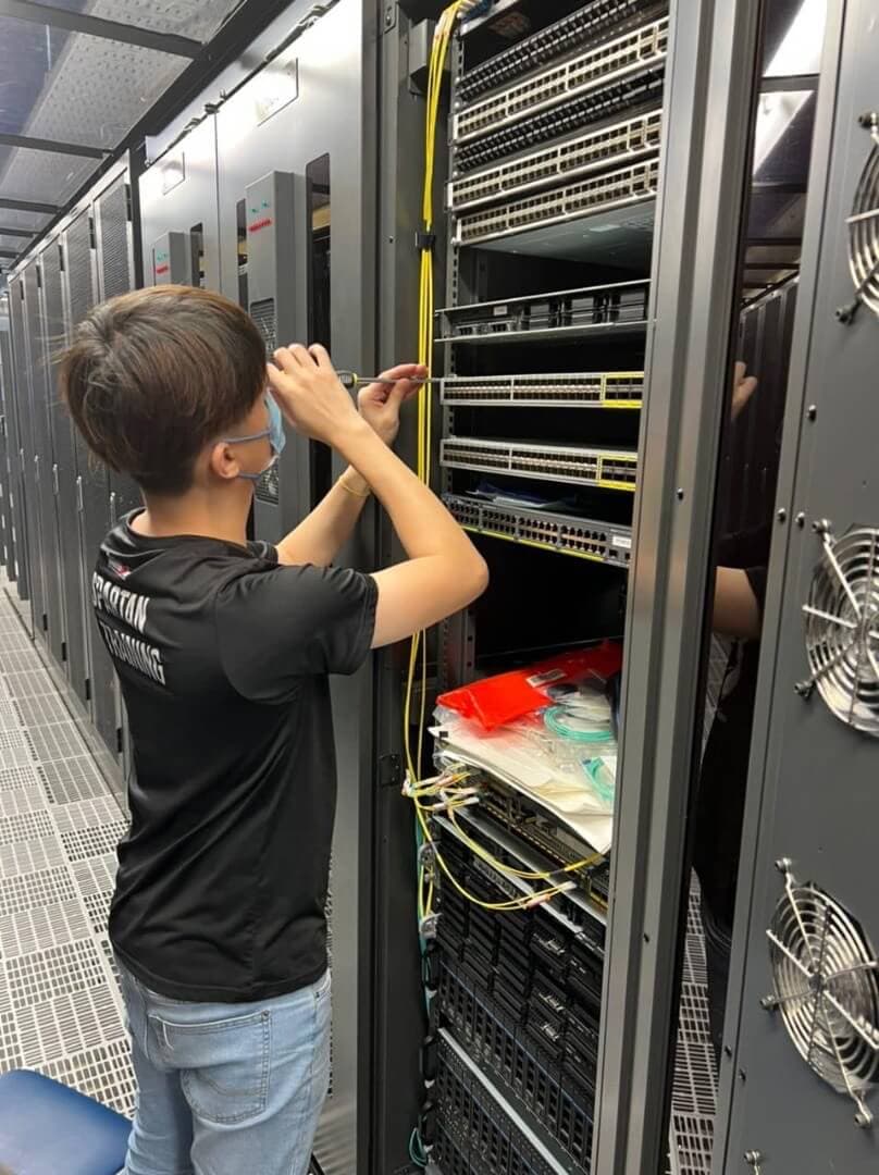 IT technician performing maintenance on network equipment in server rack with structured cabling system