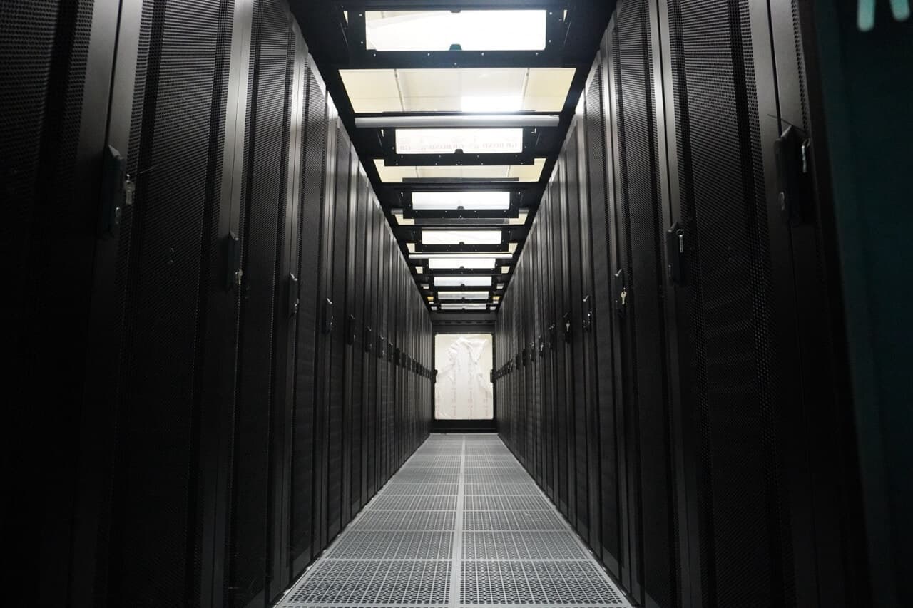 Long corridor of black server racks with raised floor and overhead lighting in enterprise data center