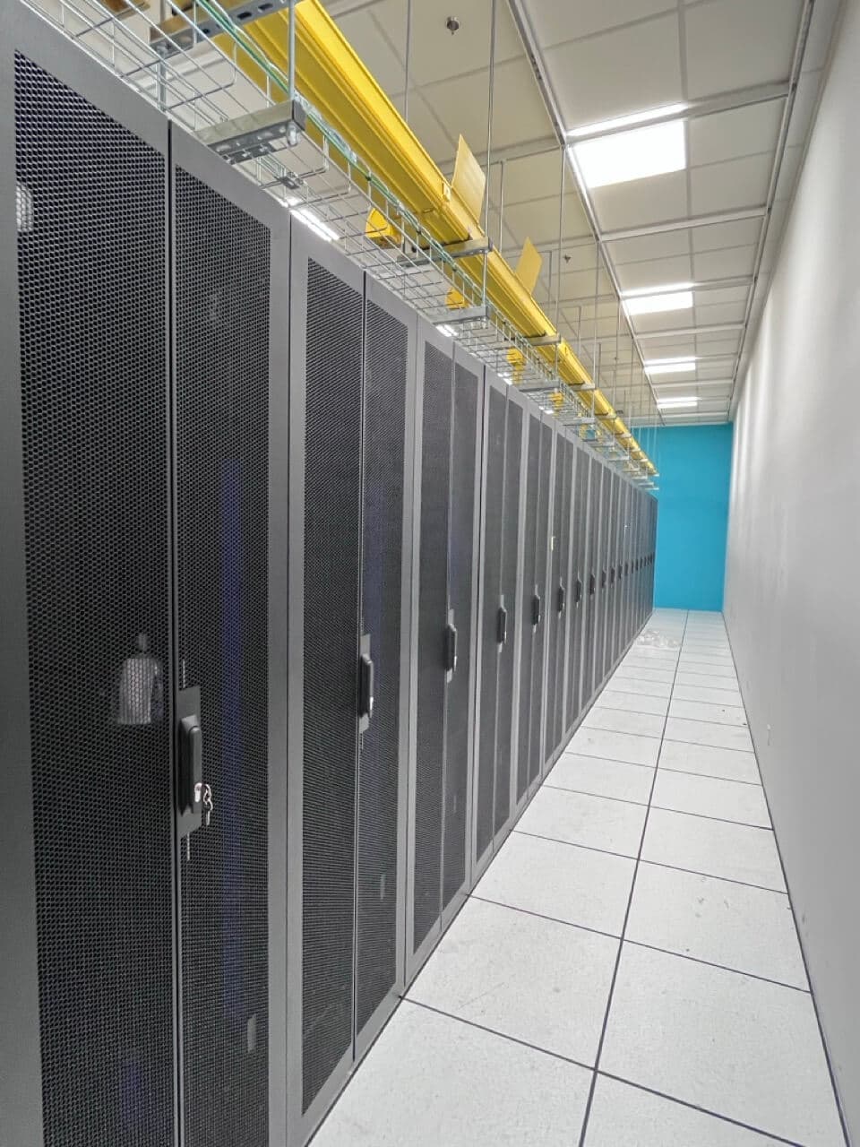 Row of server cabinets with yellow overhead cable trays in modern data center with blue accent wall