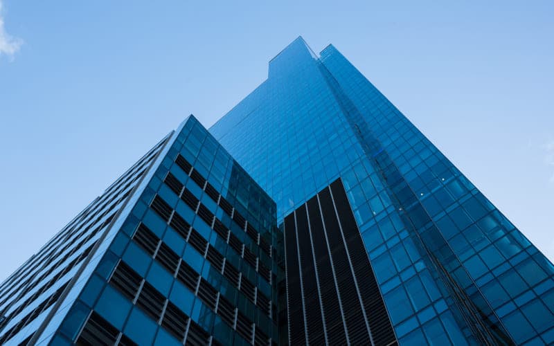 Tall glass skyscraper with reflective blue windows viewed from below against a clear sky, conveying modernity and architectural elegance.