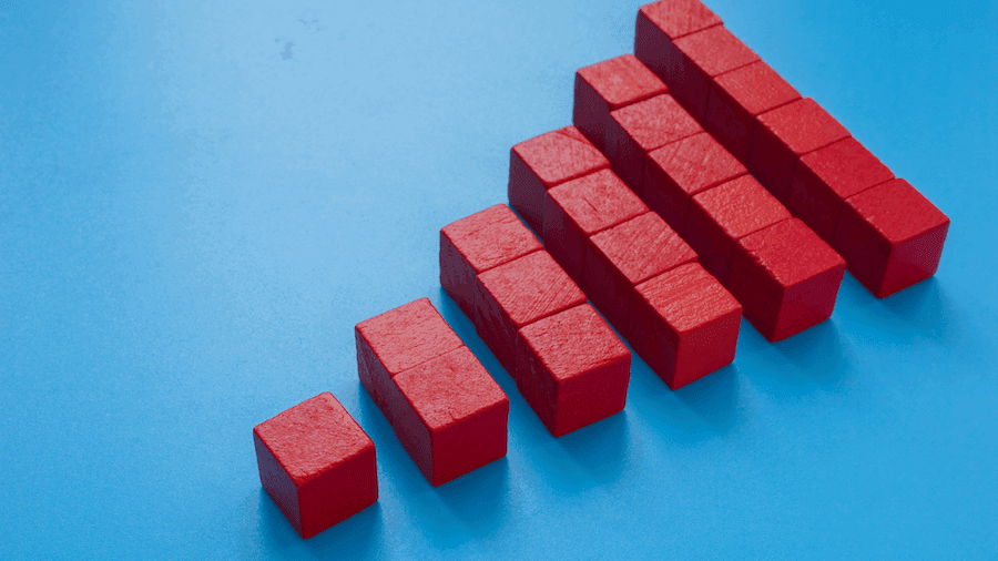Red blocks arranged in a staircase pattern on a blue background, symbolizing growth or progression. The blocks increase in size from left to right. Red blocks arranged in a staircase pattern on a blue background, symbolizing growth or progression. The blocks increase in size from left to right.