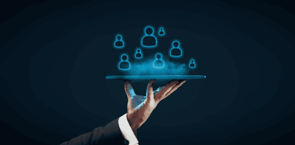 A hand in a suit holds a tablet with glowing blue icons of people floating above it, symbolizing digital connection and networking. Dark background. A hand in a suit holds a tablet with glowing blue icons of people floating above it, symbolizing digital connection and networking. Dark background.