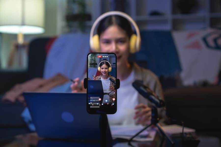 A content creator wearing headphones and holding a smartphone while streaming live, representing high-quality video streaming services. A content creator wearing headphones and holding a smartphone while streaming live, representing high-quality video streaming services.
