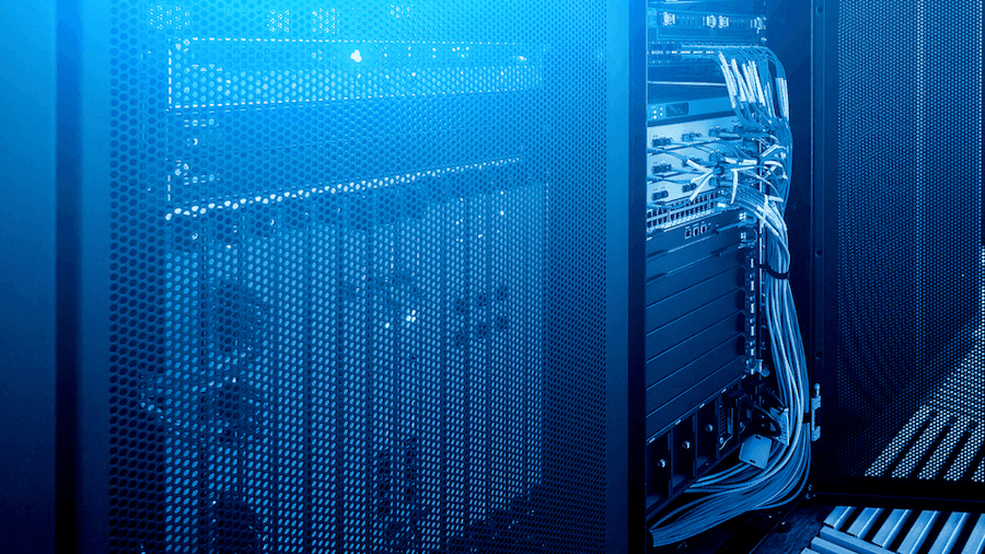 A blue-lit server room with open racks displaying network hardware and cables. The perforated casing and organized wiring suggest a high-tech environment. A blue-lit server room with open racks displaying network hardware and cables. The perforated casing and organized wiring suggest a high-tech environment.