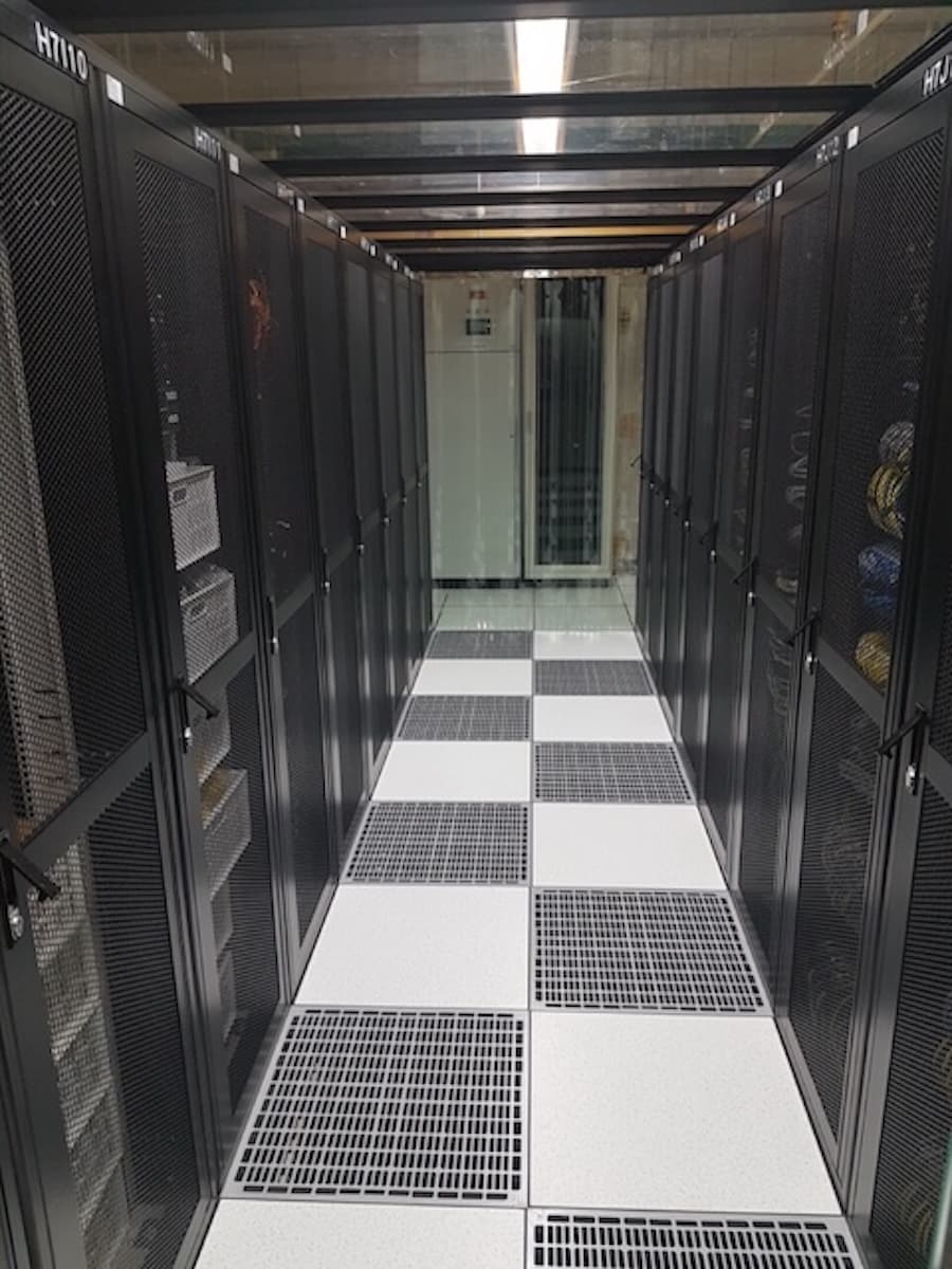 A narrow data center aisle with rows of black server racks on both sides. A narrow data center aisle with rows of black server racks on both sides.
