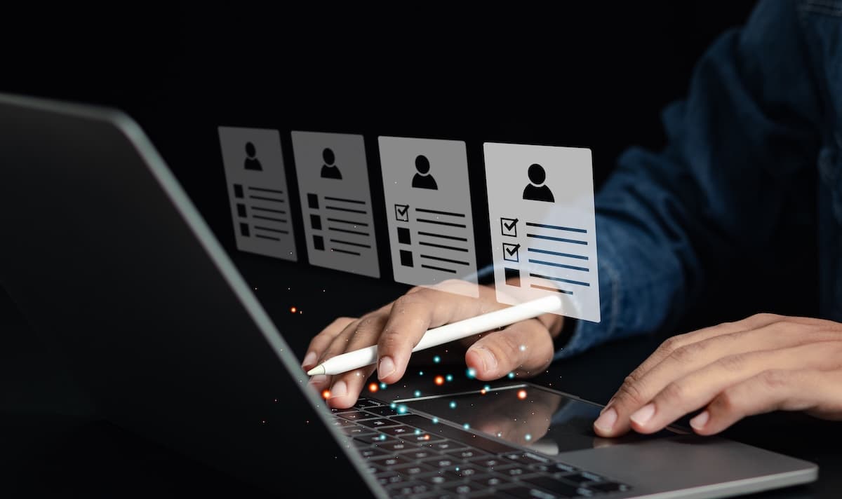 Hands use a stylus on a laptop's keyboard, interacting with floating digital profiles. Hands use a stylus on a laptop's keyboard, interacting with floating digital profiles.