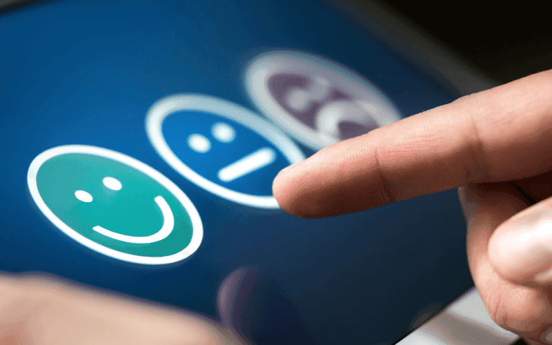 A finger hovers over three feedback icons on a touchscreen: green happy face, blue neutral face, and purple sad face, symbolizing different emotions. A finger hovers over three feedback icons on a touchscreen: green happy face, blue neutral face, and purple sad face, symbolizing different emotions.