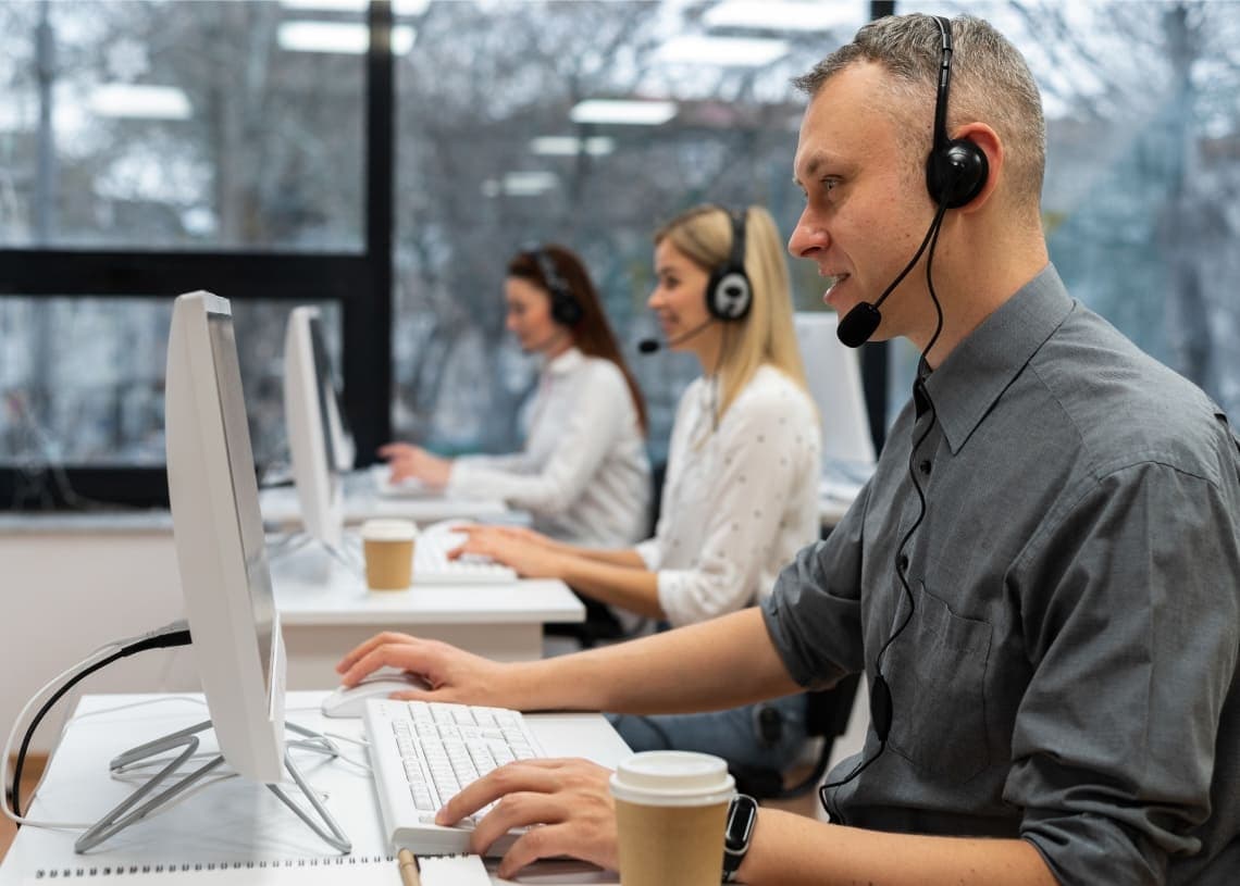 Three customer service representatives wearing headsets work at computers in a bright, modern office. They appear focused and professional. Three customer service representatives wearing headsets work at computers in a bright, modern office. They appear focused and professional.