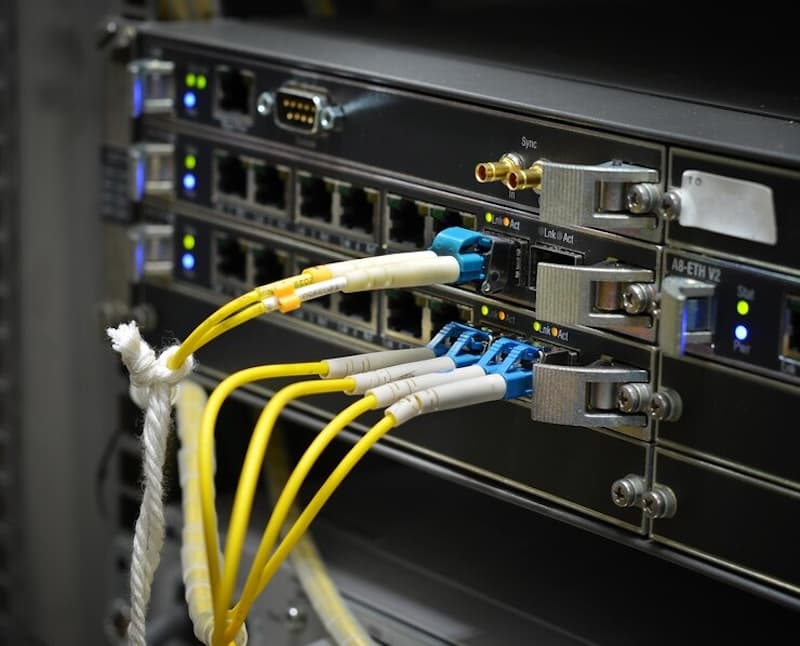 A close-up photo of network server equipment with multiple yellow fiber optic cables connected to ports. A close-up photo of network server equipment with multiple yellow fiber optic cables connected to ports.